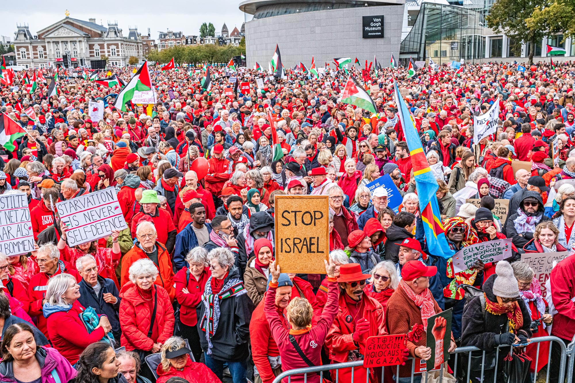 Een dicht opeengepakte menigte in het rood met Palestijnse vlaggen en borden, waaronder ‘Stop Israel’